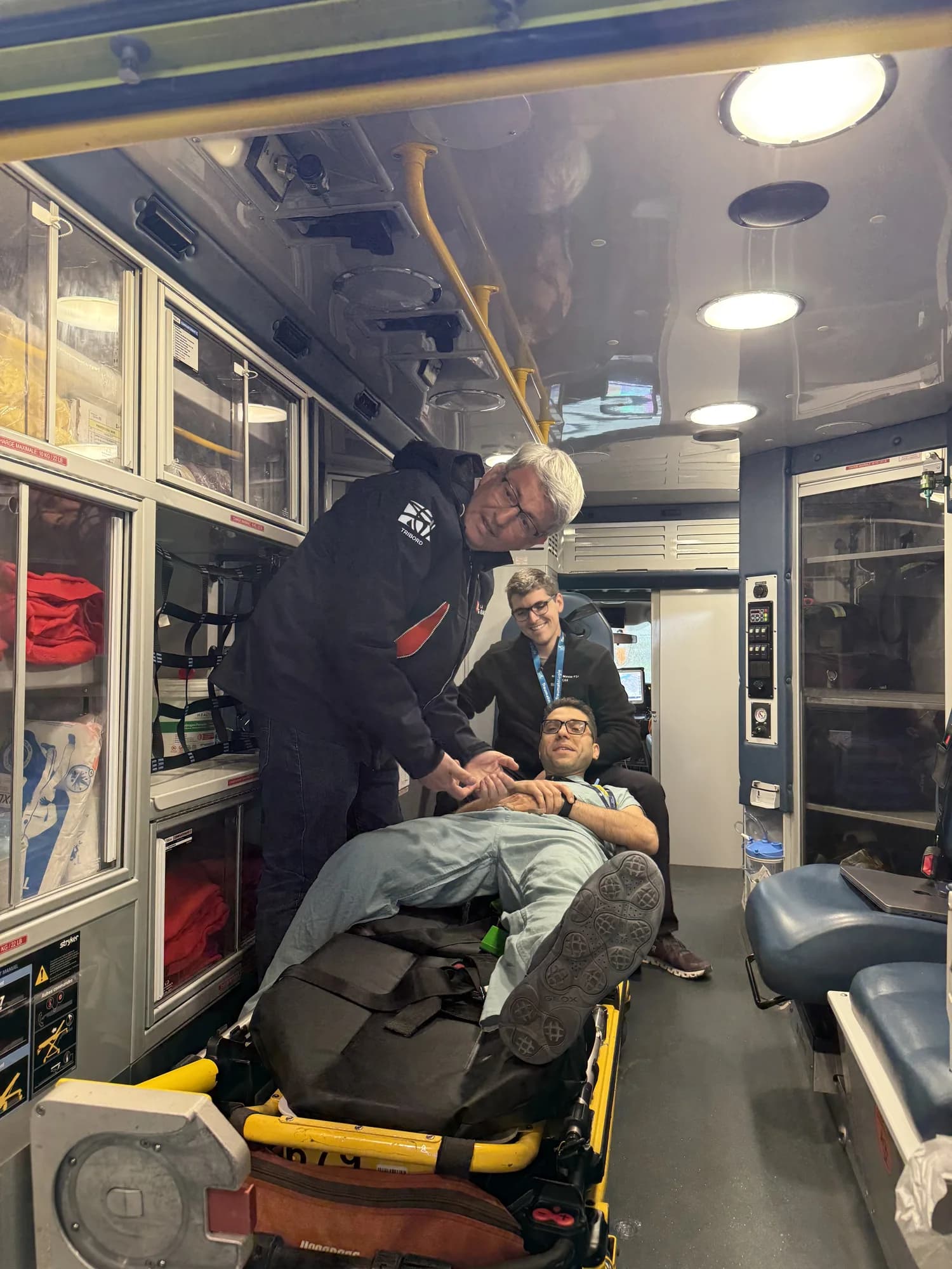 Three colleagues together inside an ambulance, one reclining on the stretcher